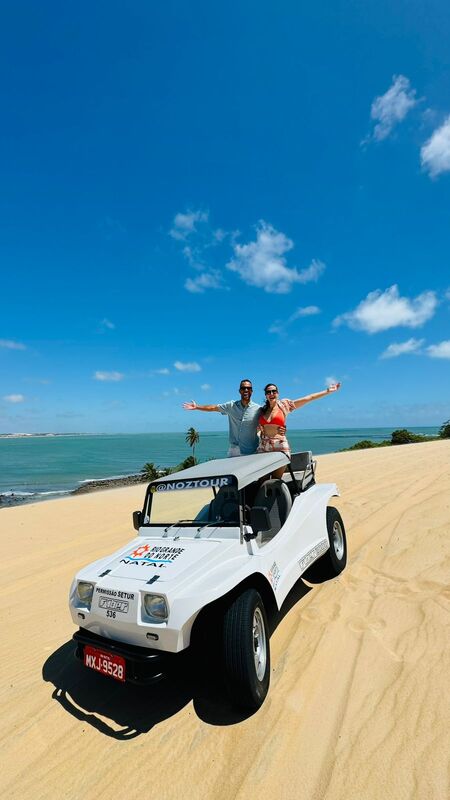 Casal no buggy nas dunas com o mar ao fundo