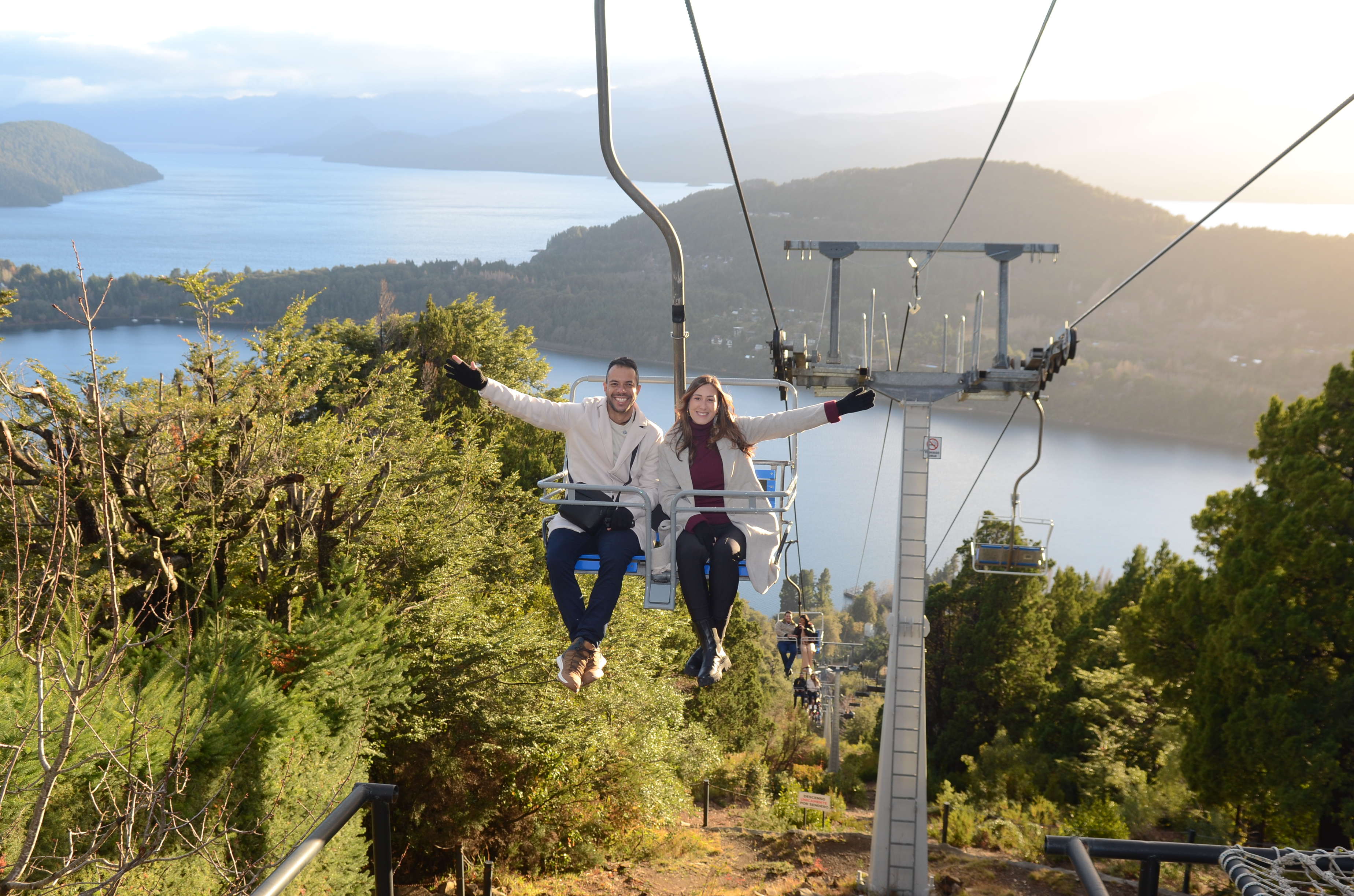Casal na aerosilla com o Lago Nahuel Huapi ao fundo, em Bariloche