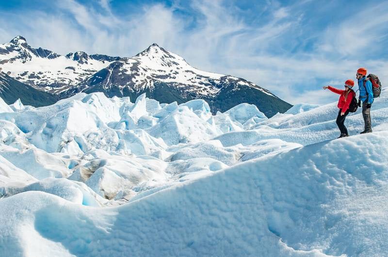 Caminhantes numa crista de gelo do Perito Moreno com montanhas ao fundo