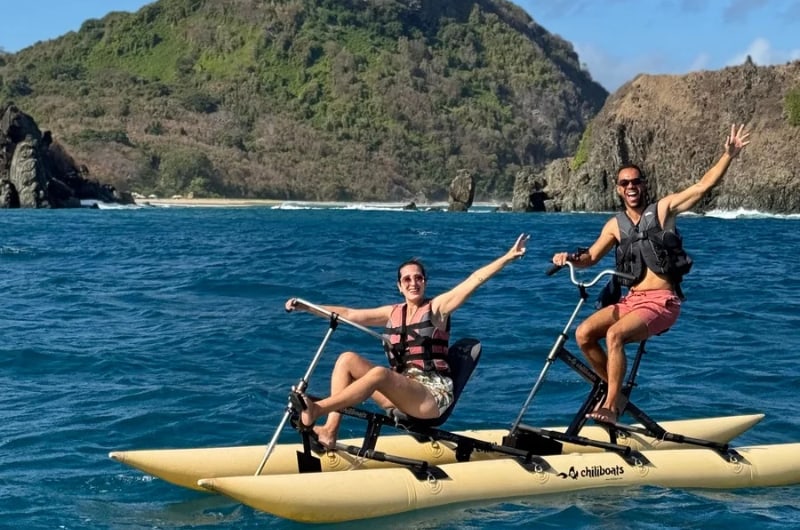 Casal pedalando bike aquática diante dos morros de Noronha