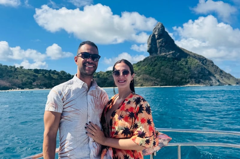 Casal no barco com o Morro do Pico ao fundo