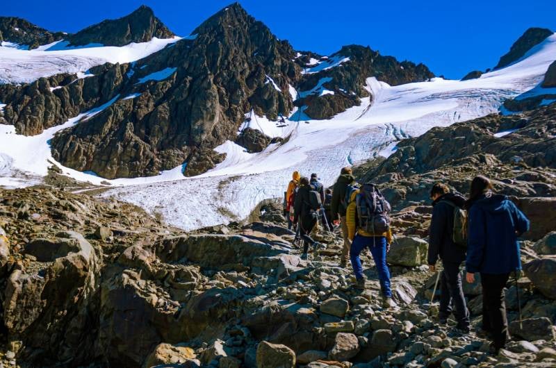 Grupo de trekking subindo a trilha com montanhas nevadas ao fundo