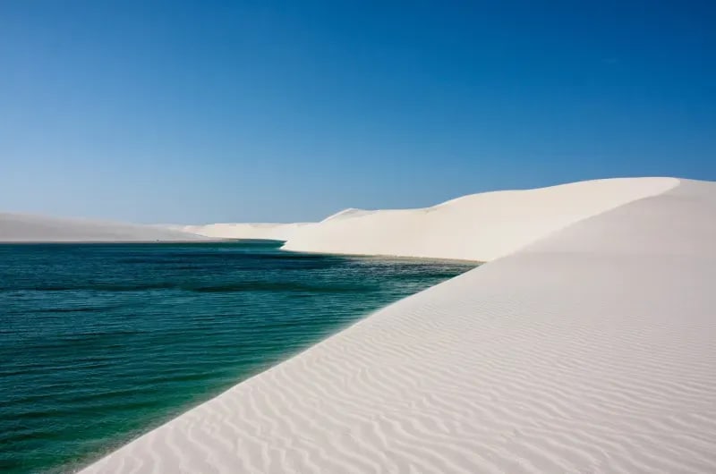 Lagoa azul funda ao lado de duna branca nos Lençóis Maranhenses