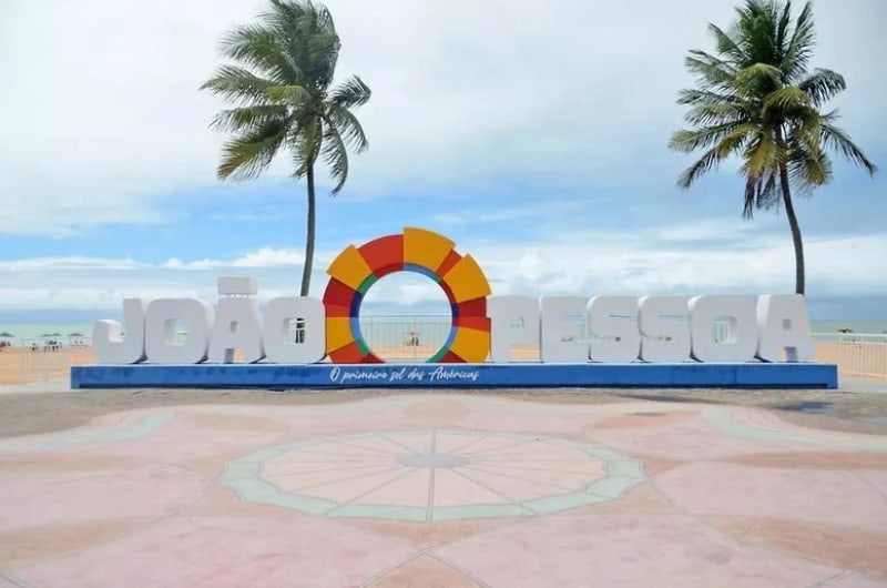 Letreiro de João Pessoa com coqueiros na orla