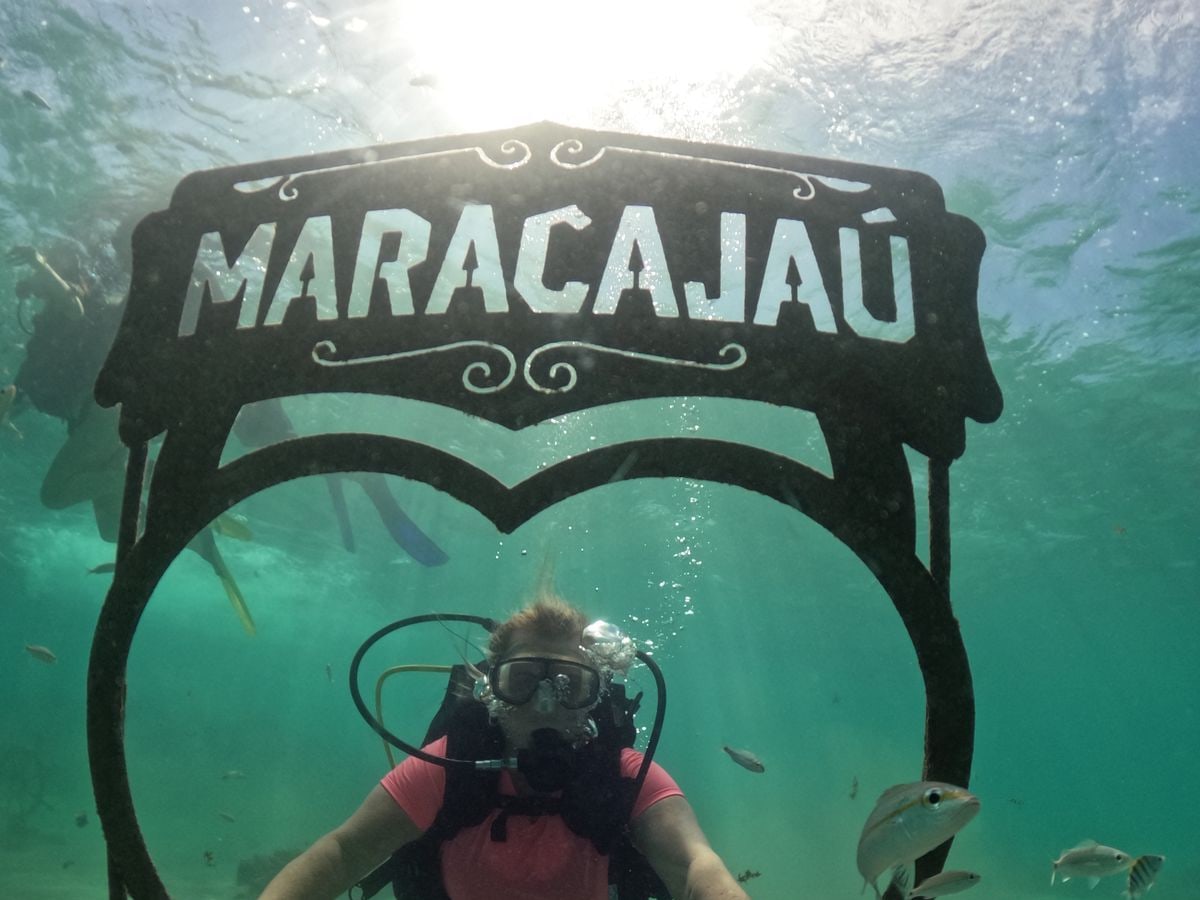 Mergulhador com cilindro embaixo da placa de Maracajaú, no fundo do mar