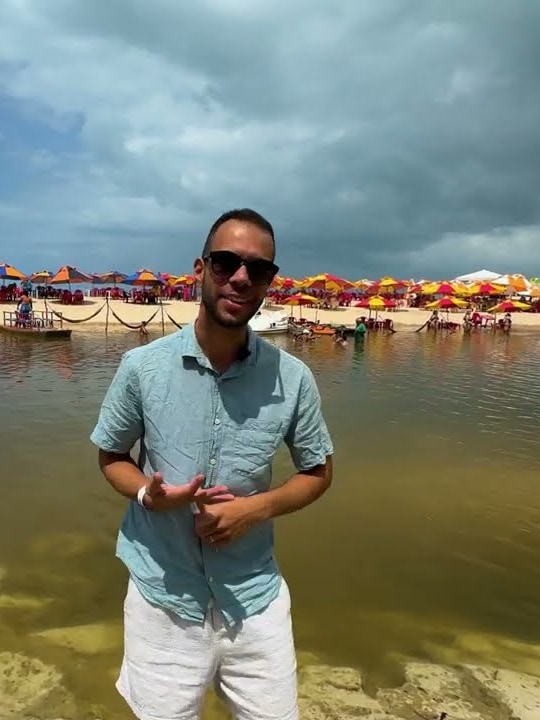 Robson na água calma da Praia Bela, com guarda-sóis coloridos ao fundo, no litoral sul da Paraíba