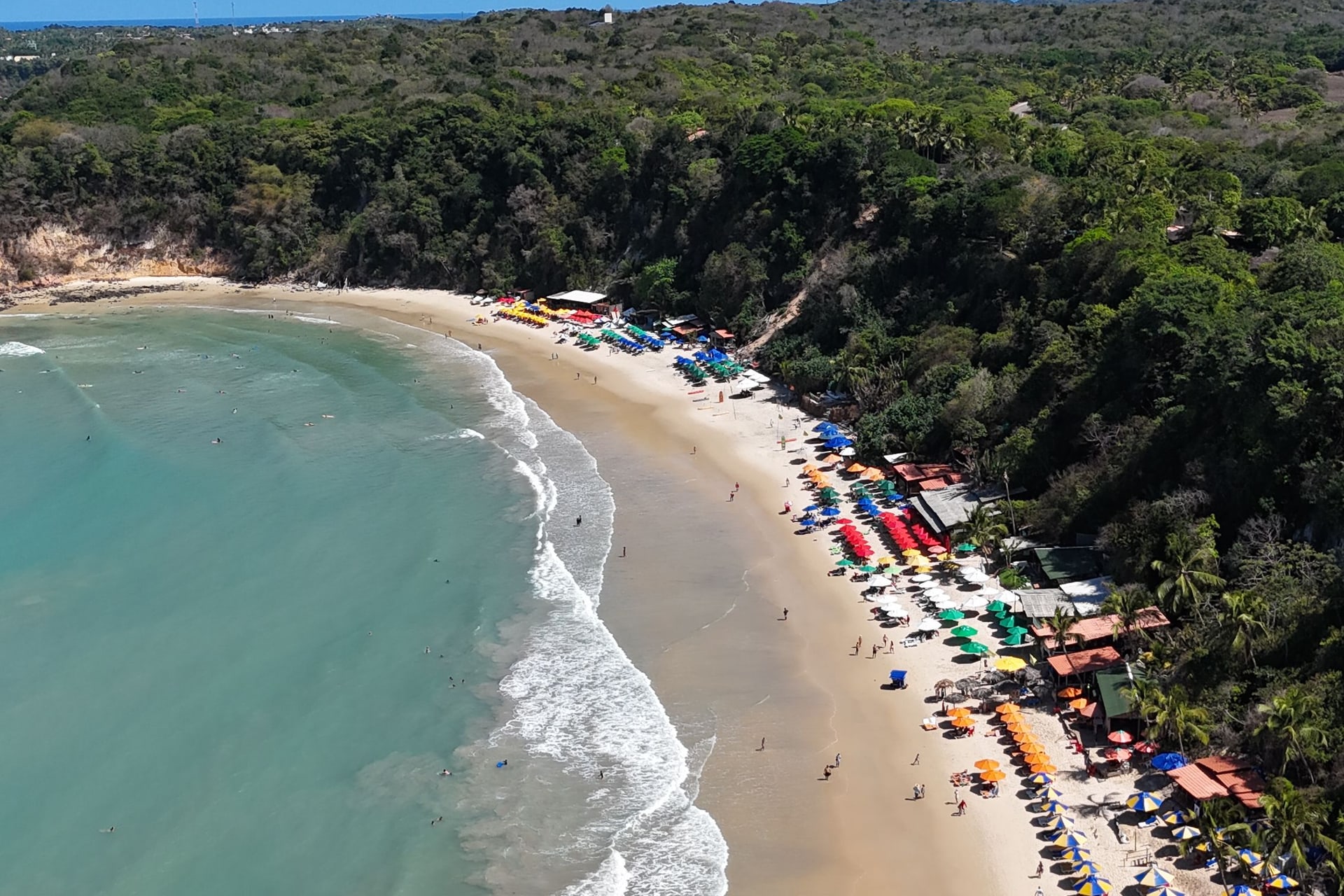 Vista aérea de uma praia de Pipa, com falésias, mata e barracas coloridas na areia