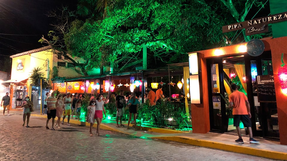 Rua movimentada do centro de Pipa à noite, com bares iluminados