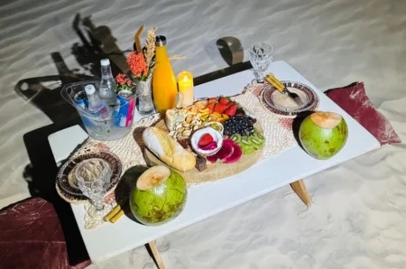 Tábua de frios e água de coco servidas na duna ao entardecer
