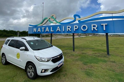 Carro do transfer da Noz Tour em frente ao letreiro do Aeroporto de Natal