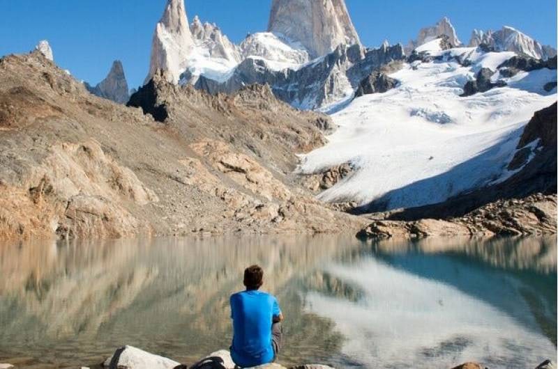 Trilheiro sentado diante do lago com o Cerro Fitz Roy refletido