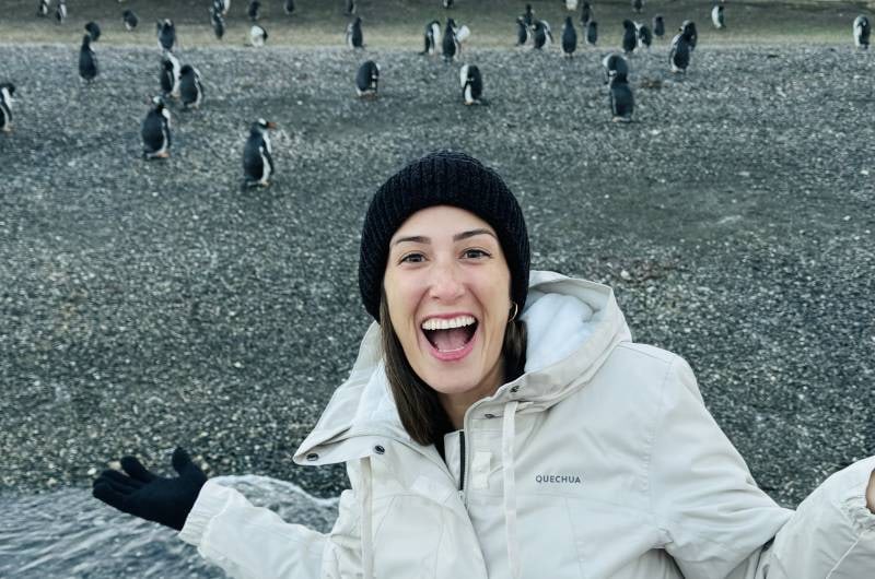 Viajante sorrindo no barco com os pinguins ao fundo