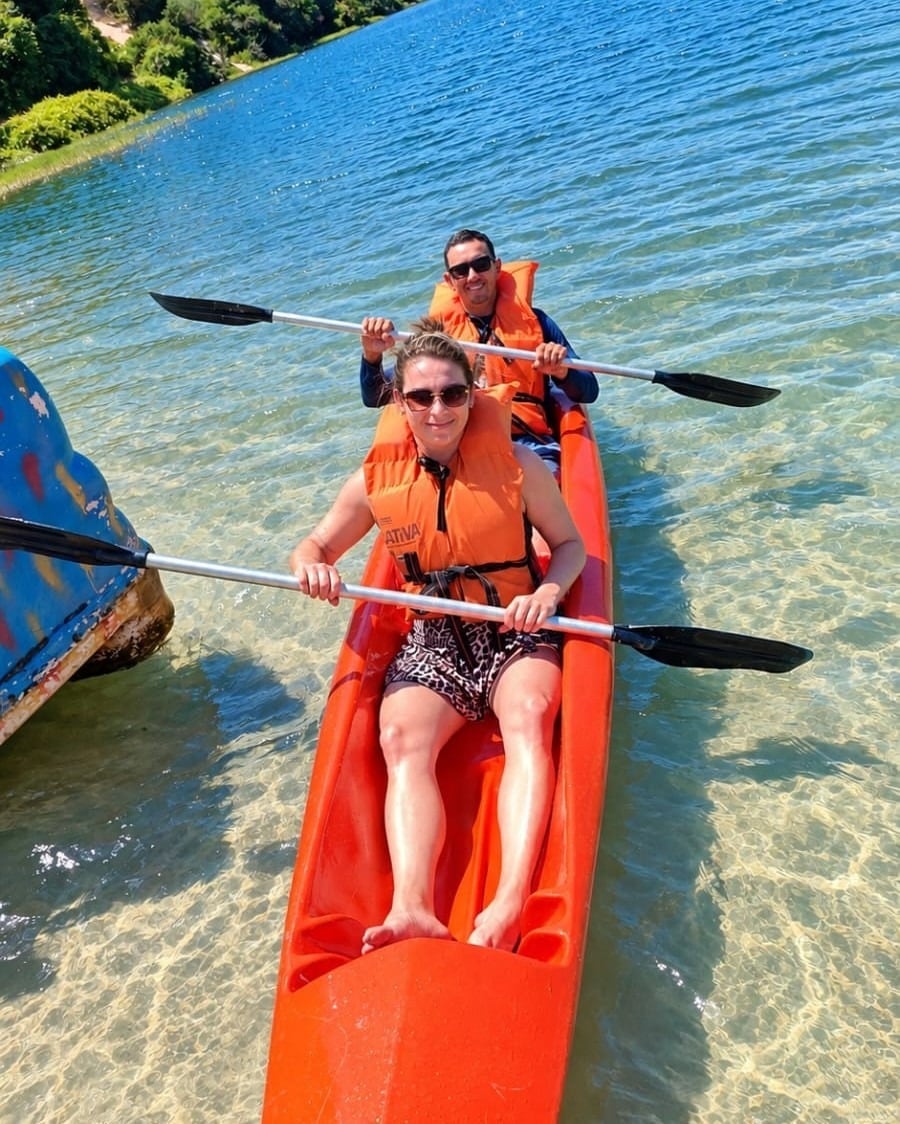 Casal de colete remando num caiaque laranja numa lagoa de água transparente e rasa