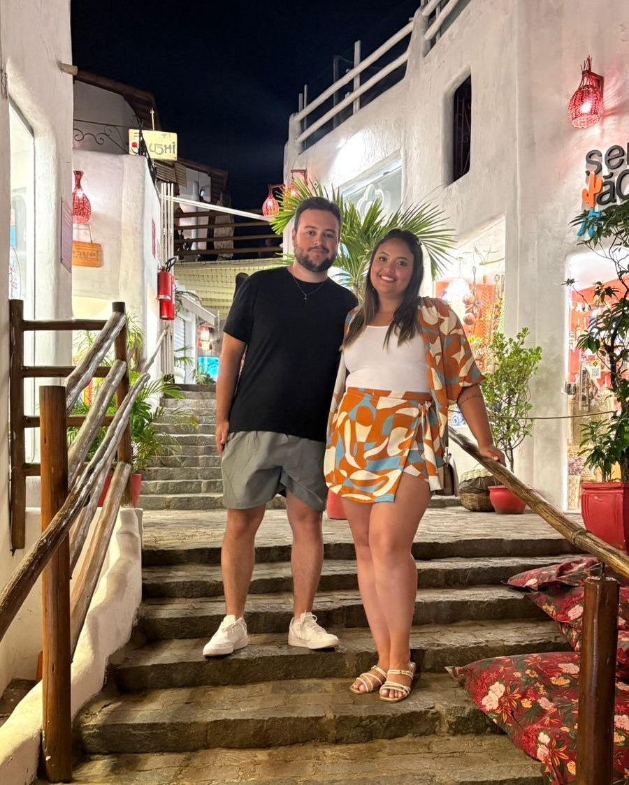 Casal na escadaria de uma galeria iluminada no centrinho de Pipa, à noite
