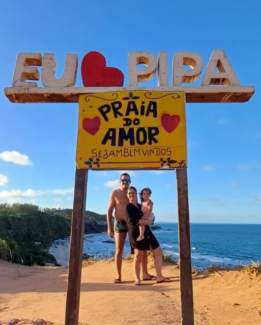 Família embaixo da placa Eu amo Pipa, Praia do Amor, com o mar e as falésias ao fundo