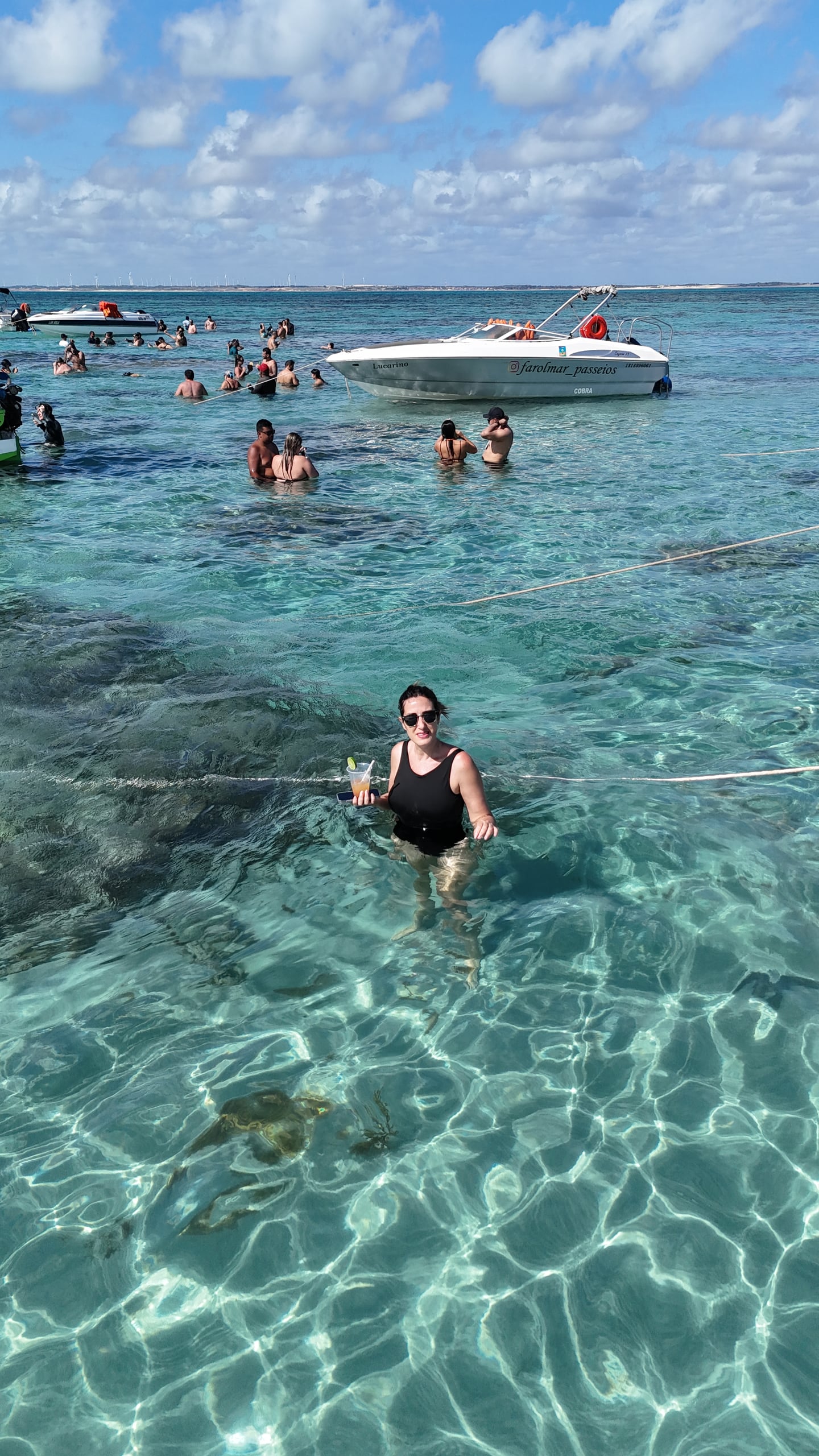 Banhistas na água transparente dos parrachos de Rio do Fogo, com lanchas ancoradas e céu de sol