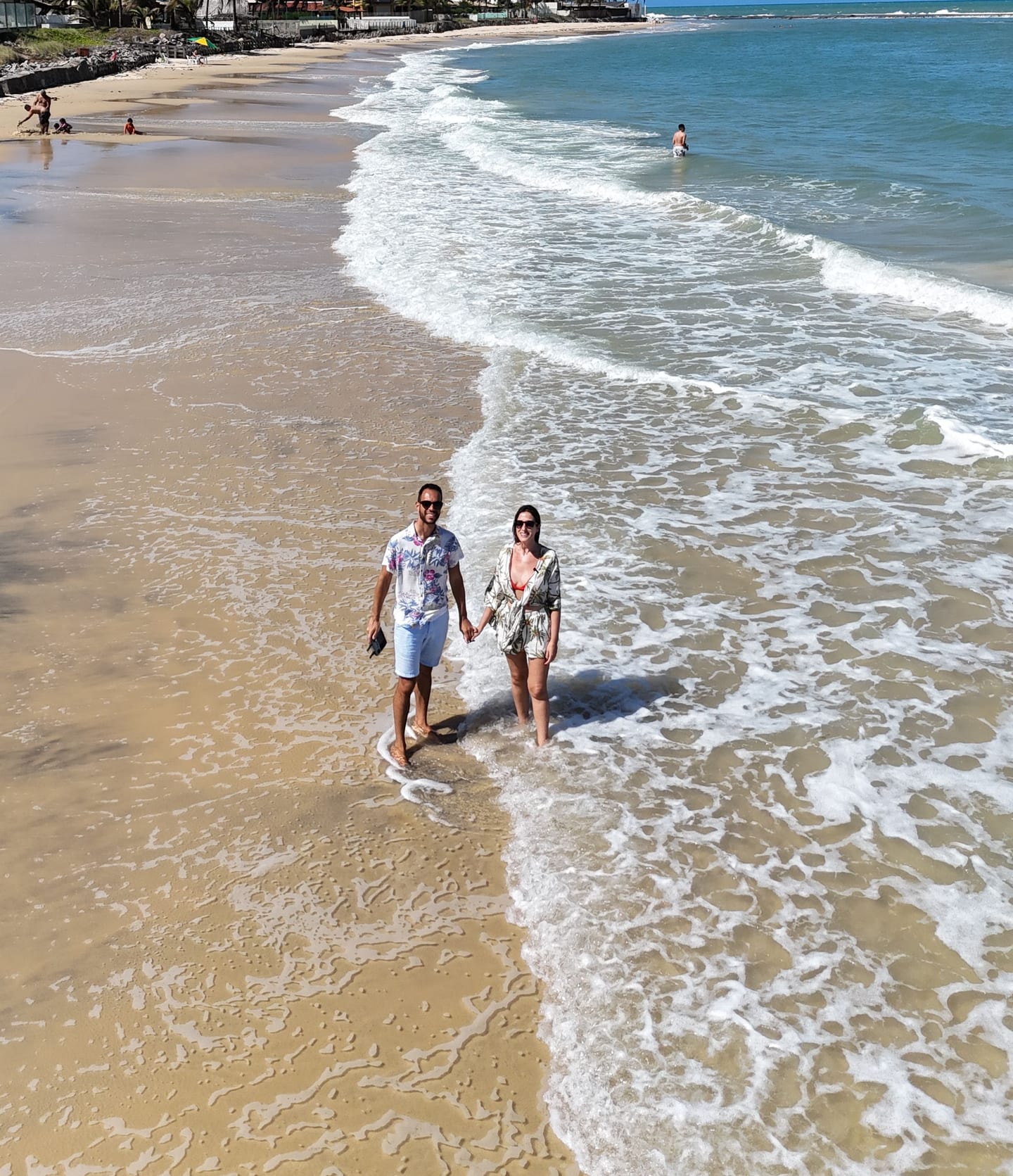Monique e Robson, da Noz Tour, de mãos dadas na beira do mar numa praia do litoral sul de Natal