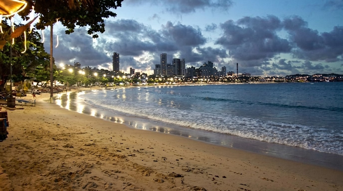 Orla iluminada no começo da noite, com a areia vazia e os prédios de Natal ao fundo