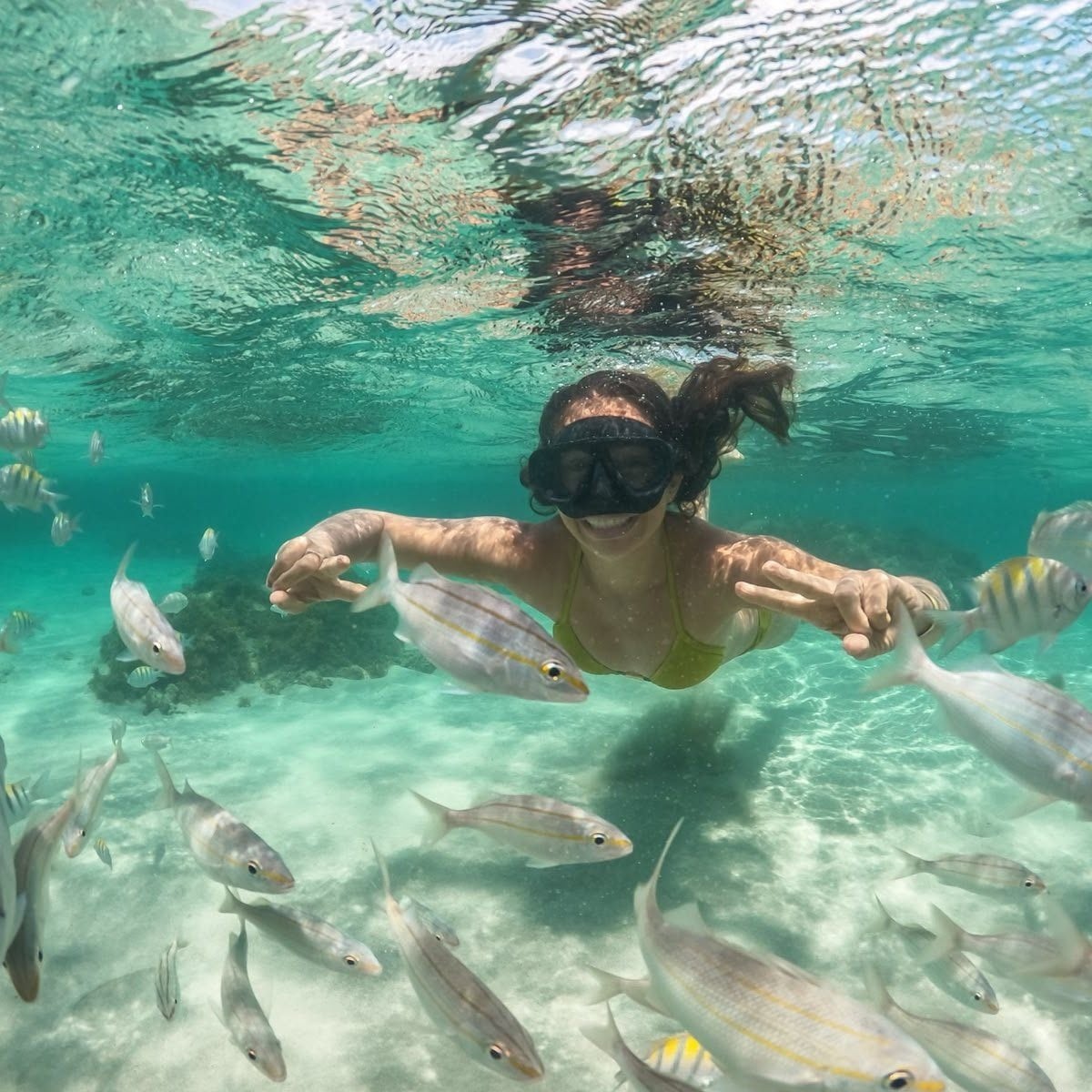 Viajante de máscara fazendo snorkel entre peixes numa piscina natural de água transparente
