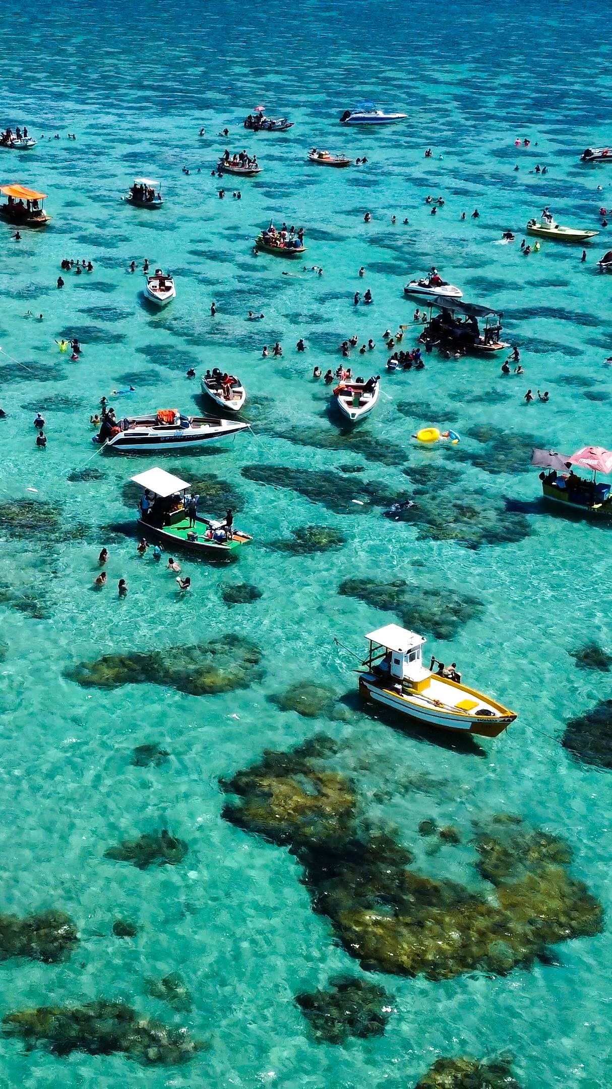 Vista aérea de lanchas e banhistas na água transparente dos parrachos de Perobas, em Rio do Fogo